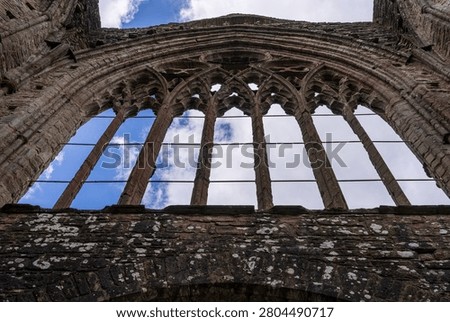 Dramatic view of the roofless nave and arched window frames of Tintern Abbey, a historic Cistercian monastery ruin in Wales.