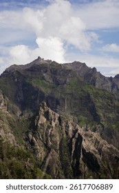 A dramatic view of a rugged green mountain peak under a partly cloudy sky, showcasing the raw beauty of Madeira's volcanic landscape.