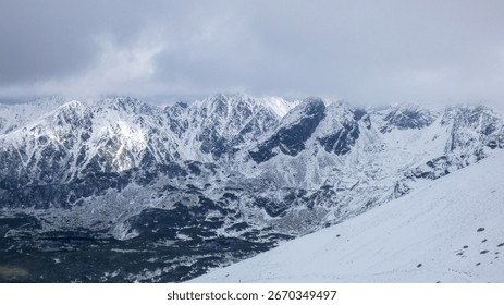 A dramatic view of a rugged mountain range covered in snow, with peaks disappearing into heavy clouds.
