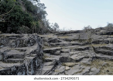 dramatic view of a sharp, jagged rockface and limestone cliffs within the kaimur hill plateau, surrounded by dense forest and morning mist near the historic rohotashgarh fort