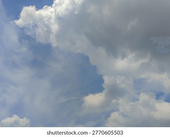 A dramatic view of the sky featuring thick, fluffy clouds partially covering the sun, with bright sun rays piercing through and creating a striking contrast against the vivid blue background. The interplay of light and shadow adds depth and a serene yet powerful atmosphere, symbolizing hope, clarity, and natural beauty. Ideal for themes related to weather, spirituality, inspiration, and nature backgrounds.