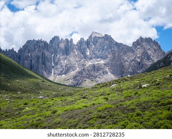 Dramatic view of snow-capped peaks and rugged cliffs at Nianbaoyuze, known as the 'Gate of Magic Realm', with a pristine alpine lake reflecting the towering mountains under a cloudy sky.
