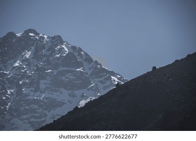 Dramatic view of the snow-capped summit of Mount Toubkal in the High Atlas Mountains of Morocco under a clear blue sky.