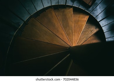 A dramatic view of a spiral wooden staircase with intricate design and warm lighting, creating a captivating and elegant architectural feature. - Powered by Shutterstock