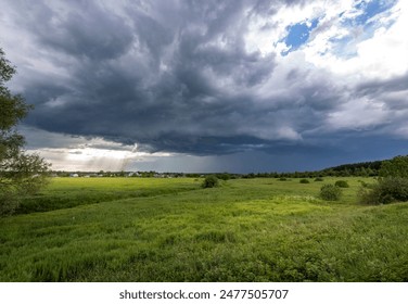 A dramatic view of storm clouds gathering over a lush green field. Sunlight pierces through the dark clouds, illuminating the landscape with an ethereal glow.