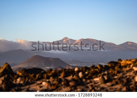 Dramatic view of the Teide volcano mountain at evening over the clouds from behind volcanic rocks at La Tejita beach in Tenerife