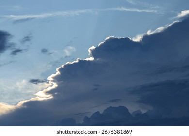 A dramatic view of thick dark clouds with sunlight shining through the blue twilight sky.