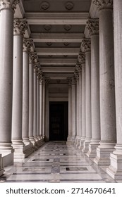 A dramatic view through a large, high arched marble doorway passage, looking down a long, dim corridor where Swiss Guards and visitors are visible in the bright distance.