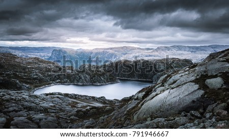 Dramatic view from the top of a mountain onto a mountain lake in front of a fjord, on a rainy September day in the norweigan highlands near Suleskard
