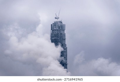 A dramatic view of a towering skyscraper shrouded in clouds, showcasing modern architecture and urban development amidst the foggy atmosphere.