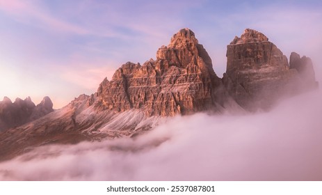 Dramatic view of Tre Cime di Lavaredo emerging through a cloud inversion at sunset or sunrise highlighting the rugged and awe-inspiring beauty of the Italian Dolomites.