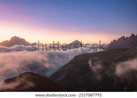 Dramatic view of Tre Cime di Lavaredo emerging through a cloud inversion at sunset or sunrise highlighting the rugged and awe-inspiring beauty of the Italian Dolomites.