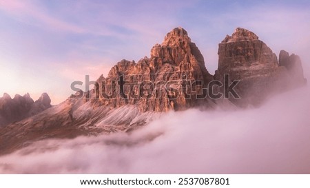 Dramatic view of Tre Cime di Lavaredo emerging through a cloud inversion at sunset or sunrise highlighting the rugged and awe-inspiring beauty of the Italian Dolomites.