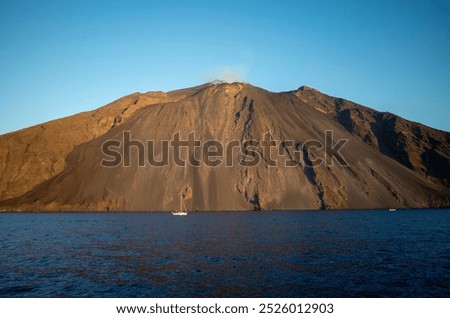 Dramatic views of Stromboli volcano rising from the Tyrrhenian Sea. Scenic seascapes featuring the iconic cone-shaped island, with sailboats and yachts adding a sense of adventure and scale.