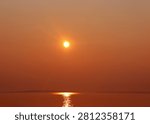Dramatic vivid orange and red sunset over Lake Superior Michigan with large glowing sun reflected on calm water surface creating stunning warm color landscape photography