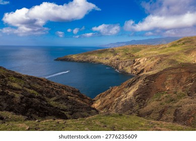 Dramatic volcanic coastline with emerald cliffs framing turquoise waters and a speedboat. Lush green hillsides overlook a sheltered cove