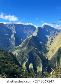 Dramatic volcanic mountain landscape on Reunion Island with deep green valleys and rugged peaks under bright blue sky. Spectacular highland scenery in the Indian Ocean, ideal for adventure travel and eco tourism concepts.