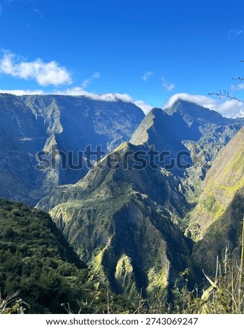 Dramatic volcanic mountain landscape on Reunion Island with deep green valleys and rugged peaks under bright blue sky. Spectacular highland scenery in the Indian Ocean, ideal for adventure travel and eco tourism concepts.