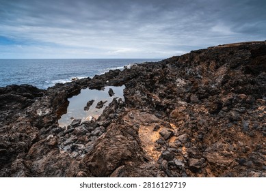 Dramatic volcanic rock formations and calm tide pools meet the vast Atlantic Ocean on a cloudy day in Buenavista del Norte