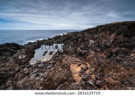 Dramatic volcanic rock formations and calm tide pools meet the vast Atlantic Ocean on a cloudy day in Buenavista del Norte