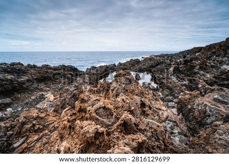 Dramatic volcanic rock formations line the shore of Tenerife, with calm tide pools reflecting the overcast sky above the vast ocean