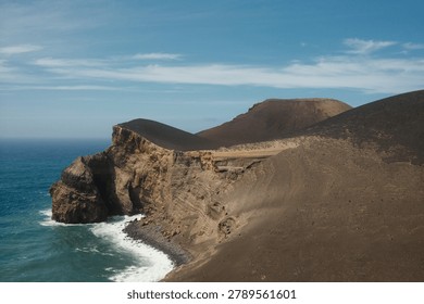 Dramatic volcanic sea cliffs with vivid layered geological strata rise above crashing Atlantic waves along a rugged coastline in the Azores, Portugal. Dark lava slopes and eroded sedimentary formations contrast sharply with the deep turquoise ocean under a partly cloudy blue sky, showcasing the raw volcanic origins of the archipelago. Ideal for travel, editorial, geotourism, and nature adventure content.