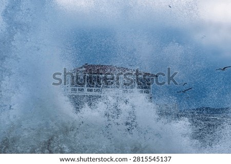 Dramatic water splash and sea spray covering a seaside building with stormy weather and birds