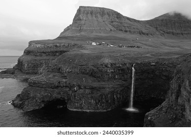 Dramatic waterfall drops from the cliffs of Gasadalur, a tiny village on the remote Faroe Islands in the black and white photo - Powered by Shutterstock