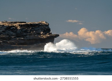 Dramatic waves smash against towering sandstone cliffs at dusk