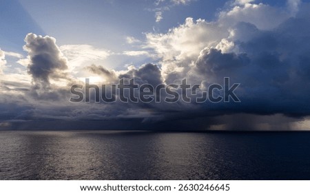 Dramatic weather clouds forming over the tranquil Pacific Ocean surface at sunset.
