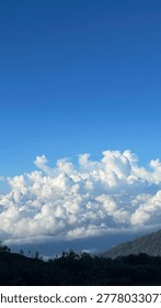 Dramatic white cloud formations under a deep blue sky above distant mountain silhouettes, capturing a peaceful natural atmosphere in daylight.