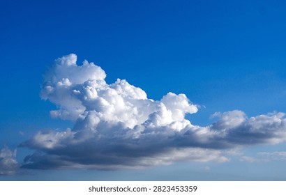 Dramatic white cumulus clouds drift across a clear blue sky in this serene natural landscape photograph capturing perfect weather conditions.