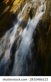 A dramatic wide waterfall flows relentlessly from gentle hills, carving its path through rugged rocks while offering a peaceful and refreshing view of nature in its purest form.