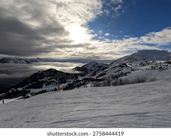 Dramatic winter landscape with sun shining through heavy clouds over a sea of fog in the valley below a ski resort with chairlifts.