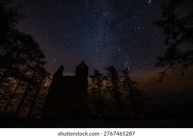 A dramatic winter night landscape beneath a star-filled sky, capturing the subtle glow of the Northern Lights over a snow-covered valley. A winding road leads through the scene, flanked by frost-laden trees illuminated with a striking red light, contrasting against the cool tones of the snow and sky. The distant horizon glows with green aurora, creating a sense of depth and quiet wilderness, while countless stars add texture and scale to this serene, remote environment.