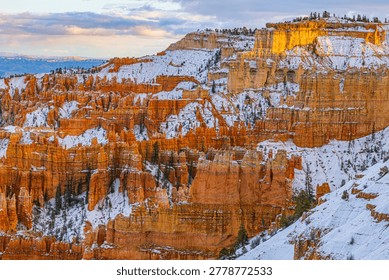 Dramatic winter scene of snow-covered red rock hoodoos and layered cliffs glowing at sunrise in Bryce Canyon National Park.