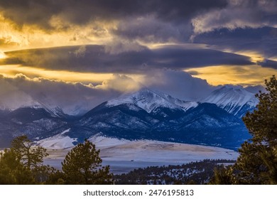 Dramatic winter sunset clouds and golden late light over the snow covered mountain peaks