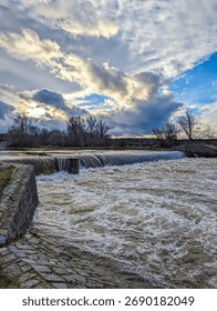 Dramatic winter sunset sky with dark clouds over flowing river and bare trees in Zatec Czech Republic. High quality photograph