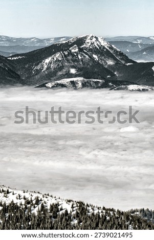 Dramatic winter view of Velky Choc mountain rising above low clouds and temperature inversion seen from Low Tatras mountains in Slovakia.