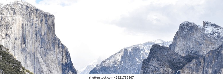 A dramatic winter view of Yosemite Valley from Tunnel View in Yosemite National Park, California, featuring El Capitan, Bridalveil Fall and snow-covered granite peaks beneath storm clouds breaking to reveal blue sky.