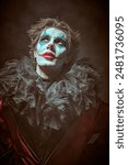 A dramatic young man - an actor with clown, joker makeup looking up to the light with tired eyes. Black background. Drama, tragedy. Performance in the theater.