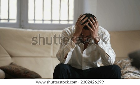 Dramatic young man feeling distraught and stressed from emotional pressure. Frustrated male person sitting at home hitting couch with hand acting aggressive