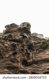 Dramatically eroded tuff rock formation rising against a pale overcast sky with sculptural layered surfaces and deep hollows