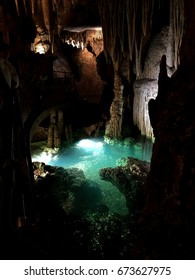 Dramatically lit scene inside a cavern with a pool of water contrasting in color with the darkish surroundings.