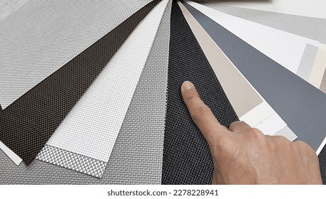 drapery catalog samples palette. architect's hand choosing samples of roller blind fabrics in different textures and colors, close up view. roman curtain fabrics samples swatch for home decoration.  - Shutterstock ID 2278228941