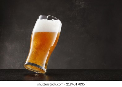 Draught beer in glass on a black slate table and dark background. Tilted glass of fresh and cold beer on gray dark background. Selective focus - Shutterstock ID 2194017835