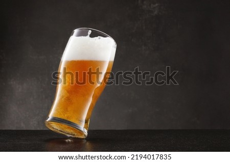 Draught beer in glass on a black slate table and dark background. Tilted glass of fresh and cold beer on gray dark background. Selective focus