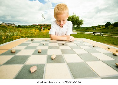 Draughts Board Game. Little Boy Clever Child Kid Playing Checkers Thinking, Outdoor In The Park. Childhood And Development