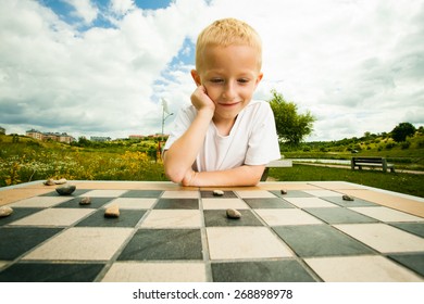 Draughts Board Game. Little Boy Clever Child Kid Playing Checkers Thinking, Outdoor In The Park. Childhood And Development