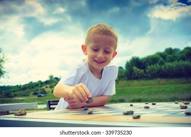 Draughts Board Game. Little Boy Clever Child Kid Playing Checkers Thinking Outdoor In The Park. Childhood And Development